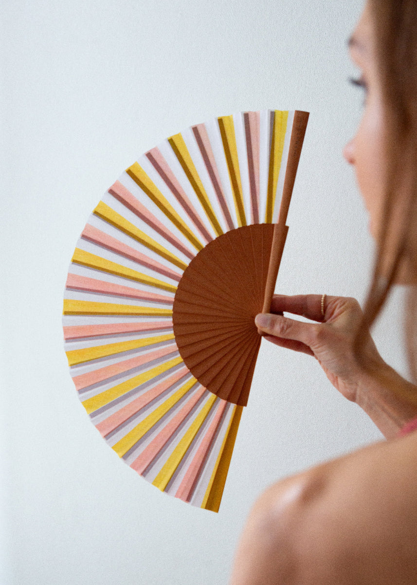 Person holding a colorful hand fan with a plain background