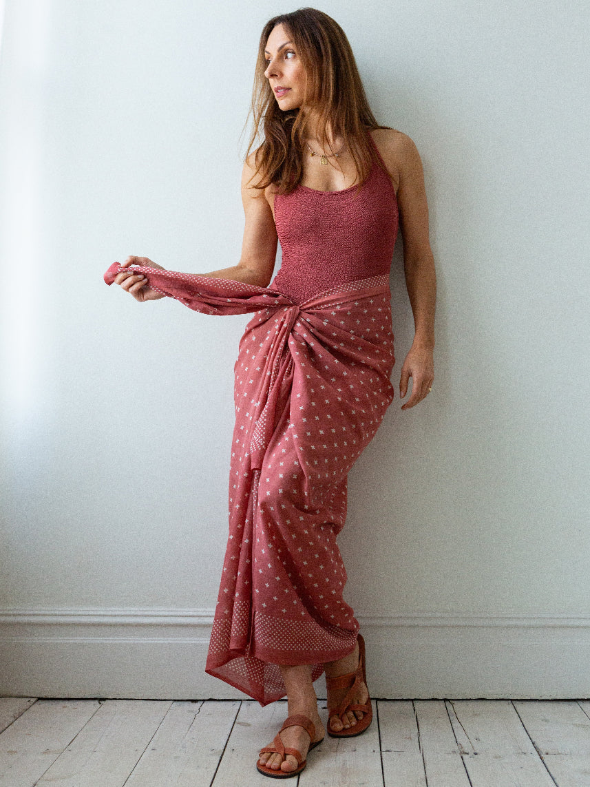 Woman wearing a pink polka dot dress against a white wall.
