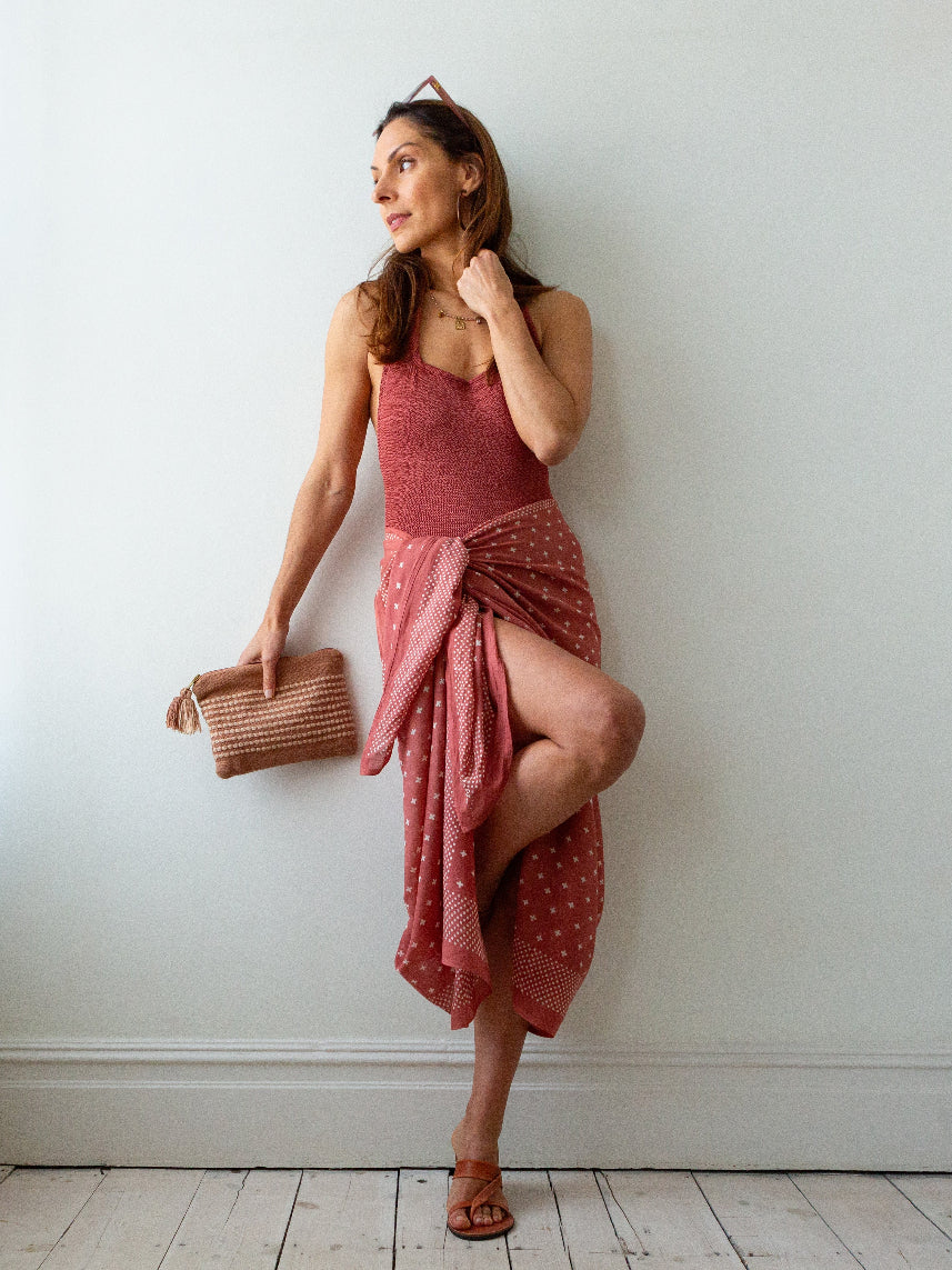 Woman in a red dress holding a brown bag against a white wall