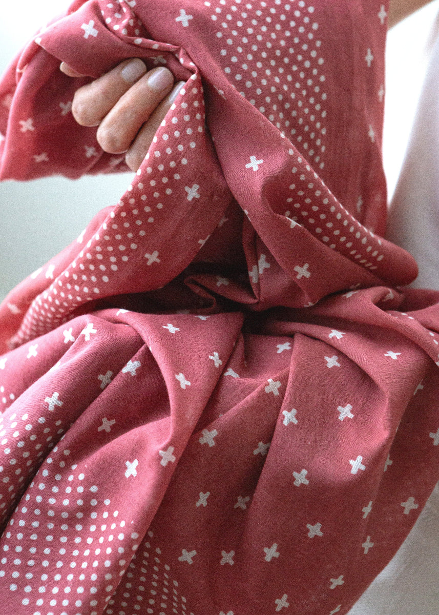 Close-up of a red fabric with white patterns held by a hand.