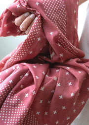 Close-up of a red fabric with white patterns held by a hand.