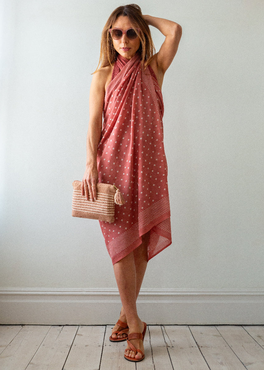 Woman wearing a red polka dot dress holding a beige clutch against a white wall.