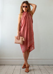 Woman wearing a red polka dot dress holding a beige clutch against a white wall.