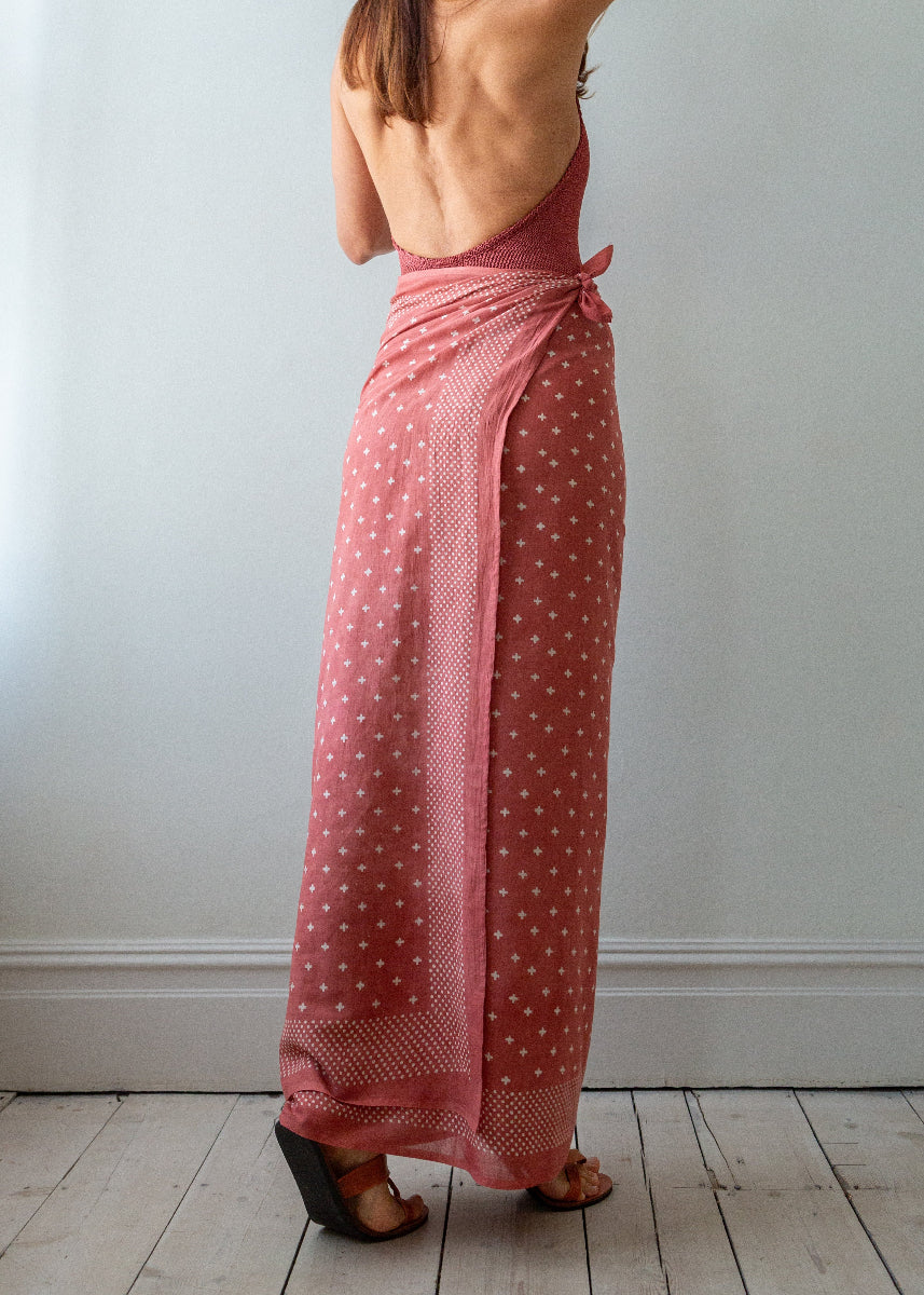 Person wearing a pink polka dot sarong against a white wall.