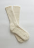 A pair of cream-colored ribbed knit crew alpaca socks laid flat on a light gray background.