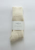 A pair of cream-colored knit alpaca socks bundled with a white paper label that reads 'THE SMALL SHOP', set against a plain white background.