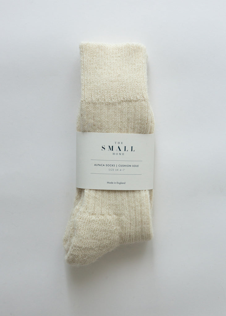 A pair of cream-colored knit alpaca socks bundled with a white paper label that reads 'THE SMALL SHOP', set against a plain white background.