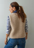A woman shown from the back wearing a beige sherpa fleece vest over a navy and white striped long-sleeve shirt, paired with blue jeans, against a plain light gray background.