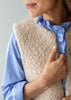 Close-up of a woman wearing a cream-colored sherpa fleece vest over a blue and white striped shirt.