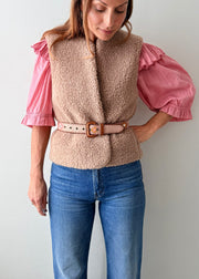 A close-up of a person wearing a pink knit sweater, blue jeans, and a decorative Guatemalan belt with a brown leather buckle. The belt has a tan base with colorful geometric patterns in orange, yellow, and white.