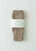A pair of folded ribbed knit socks in a heathered taupe-brown color, wrapped with a white paper label that reads 'THE SMALL HOME'. The product is photographed flat on a clean, light off-white background.