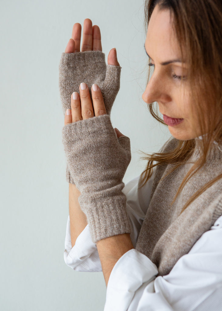 A woman wearing beige knit fingerless gloves and a matching knit sweater vest, shown from the side against a plain light gray background.