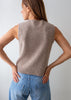 A woman shown from the back wearing a sleeveless ribbed knit sweater vest in a warm taupe-beige color, paired with light blue jeans, against a plain light gray background.