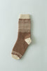 A single brown knit sock with cream-colored toe, heel, and cuff details, featuring a cream and brown geometric pattern around the calf, laid flat on a light gray background.