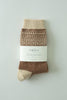 A pair of knit socks in brown and beige, wrapped in a white paper band labeled 'the SMALL lot', photographed flat against a light gray background.
