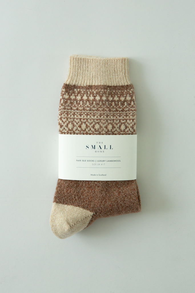 A pair of knit socks in brown and beige, wrapped in a white paper band labeled 'the SMALL lot', photographed flat against a light gray background.
