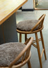 Two wooden bar stools with round, shaggy taupe-gray cushions, positioned next to a light wood counter in a modern interior setting.