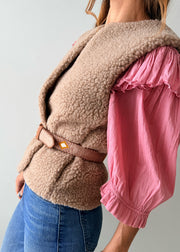 A close-up of a person wearing a pink knit sweater, blue jeans, and a decorative Guatemalan belt with a brown leather buckle. The belt has a tan base with colorful geometric patterns in orange, yellow, and white.