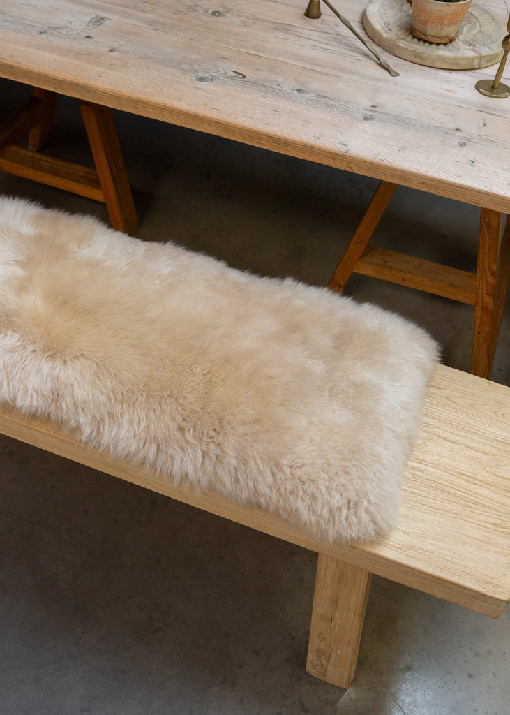 A light beige sheepskin bench cover draped over a light wood bench in a rustic dining room setting.