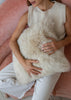A person seated on a pink upholstered chair holding a sheepskin pillow in cream or off-white.
