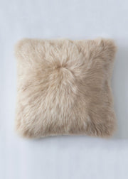 A square sheepskin throw pillow in a light beige color, photographed from directly above on a light gray background.