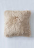 A square sheepskin throw pillow in a light beige color, photographed from directly above on a light gray background.