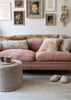 A dusty pink fabric sofa in a cozy living room setting, styled with sheepskin throw pillows, a matching sheepskin ottoman, and neutral slippers on a light wood floor.