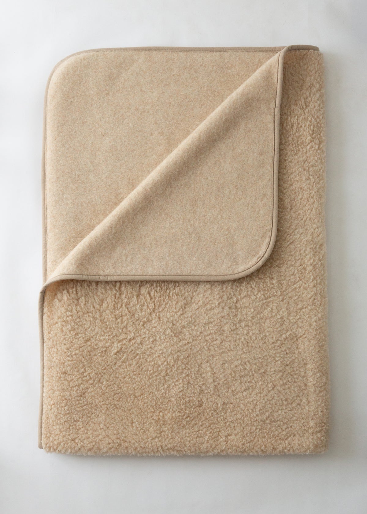 A folded beige fleece blanket with a matching fabric pocket on one corner, shown on a light off-white background.