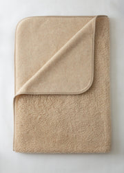 A folded beige fleece blanket with a matching fabric pocket on one corner, shown on a light off-white background.