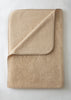 A folded beige fleece blanket with a matching fabric pocket on one corner, shown on a light off-white background.