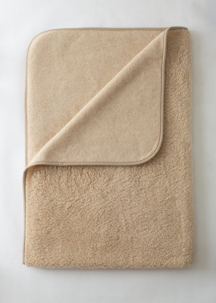 A folded beige fleece blanket with a matching fabric pocket on one corner, shown on a light off-white background.