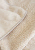 Close-up of a soft cream-colored sherpa fleece blanket with a smooth fabric edge.