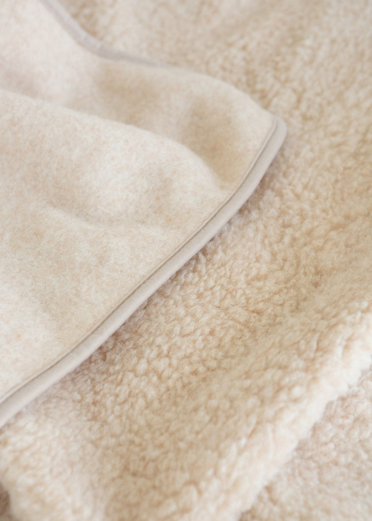 Close-up of a soft cream-colored sherpa fleece blanket with a smooth fabric edge.