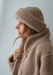 A woman in profile wearing a cozy taupe merino fleece beanie and matching fleece jacket against a plain light gray background.