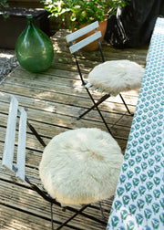 Two outdoor folding chairs with round, fluffy cream sheepskin seats on a wooden deck, next to a patterned tablecloth.
