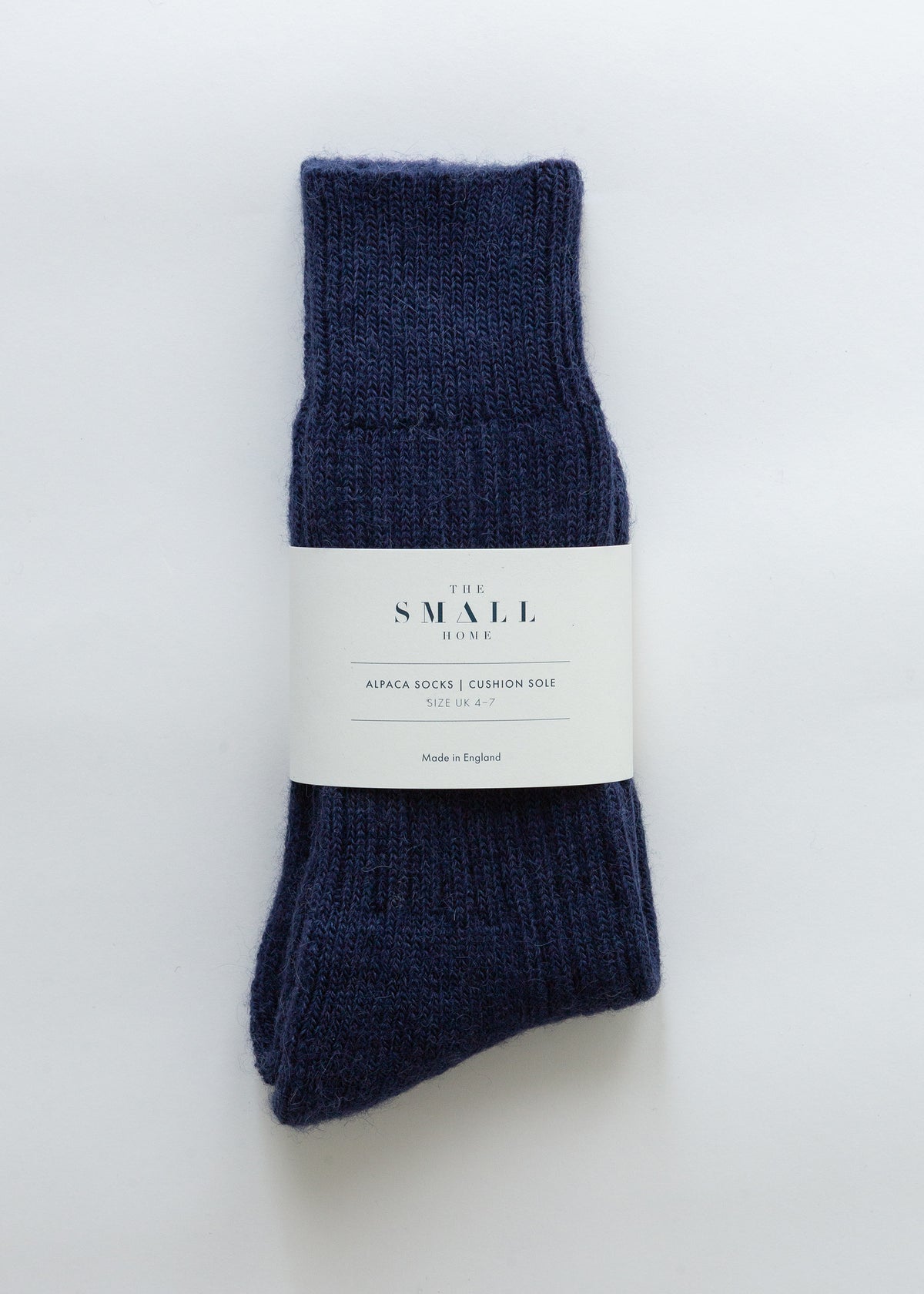 A pair of dark navy blue ribbed knit alpaca socks bundled with a white paper label that reads 'THE SMALL HOUSE'.