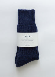 A pair of dark navy blue ribbed knit alpaca socks bundled with a white paper label that reads 'THE SMALL HOUSE'.