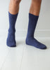 A pair of dark navy blue ribbed knit crew alpaca socks worn on a person's legs, standing on a white wooden floor against a white wall.