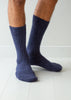 A close-up of a person's lower legs wearing dark navy blue ribbed wool alpaca socks on a white wooden floor.