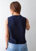 A woman shown from the back wearing a sleeveless navy knit sweater vest over a light blue top, paired with light wash blue jeans, against a plain light gray background.