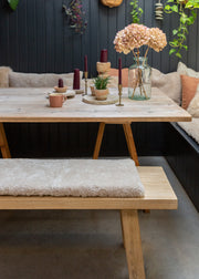 A rustic wooden dining table with matching bench seats in a cozy indoor setting, decorated with candles, a small plant, and a vase of dried flowers against a dark paneled wall.