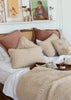 Two textured merino wool cushions in cream on a bed with a matching wool bedspread