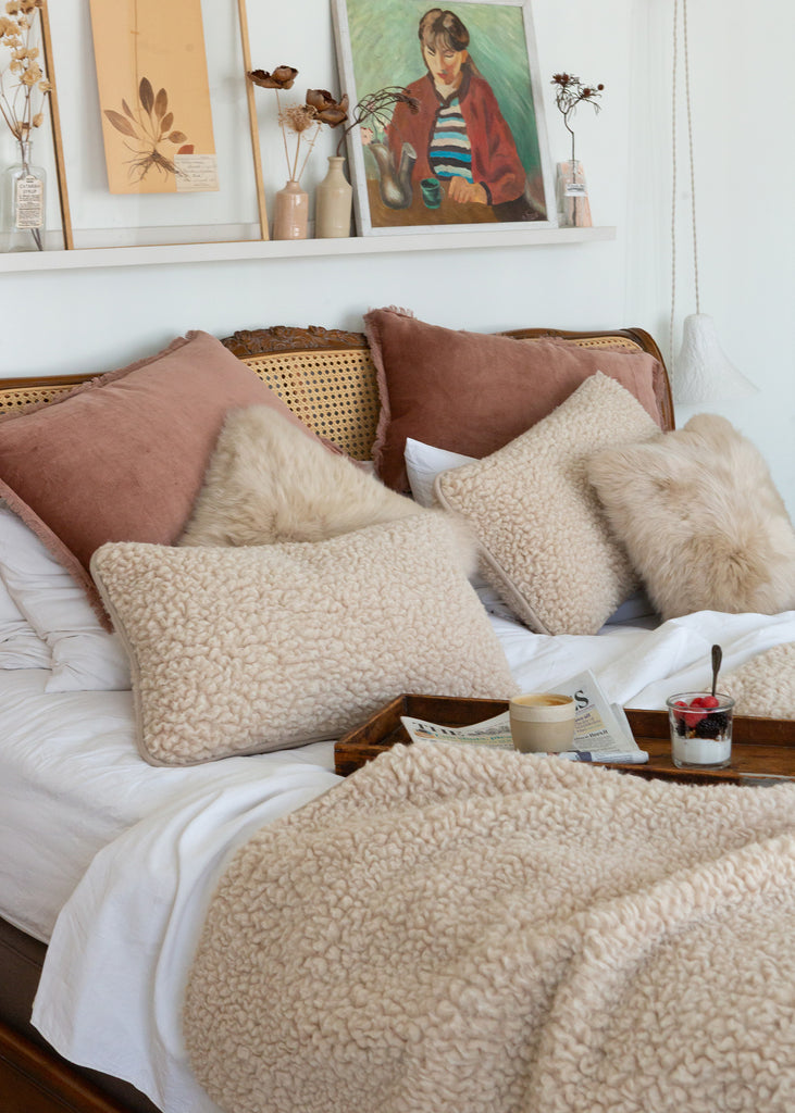 Two textured merino wool cushions in cream on a bed with a matching wool bedspread