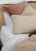 Two textured merino wool cushions in cream on a bed with a matching wool bedspread