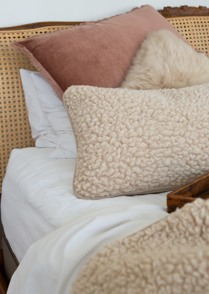 Two textured merino wool cushions in cream on a bed with a matching wool bedspread