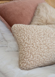 Two textured merino wool cushions in cream on a bed with a matching wool bedspread