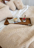 A cozy bedroom scene with cream sherpa bedding, including a textured blanket, pillows, and duvet, styled with a wooden tray holding a newspaper, a small cup, and a yogurt bowl on a bed with white sheets.