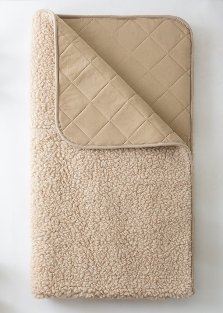 A folded beige sherpa fleece blanket with a quilted reverse side, shown on a clean white background.