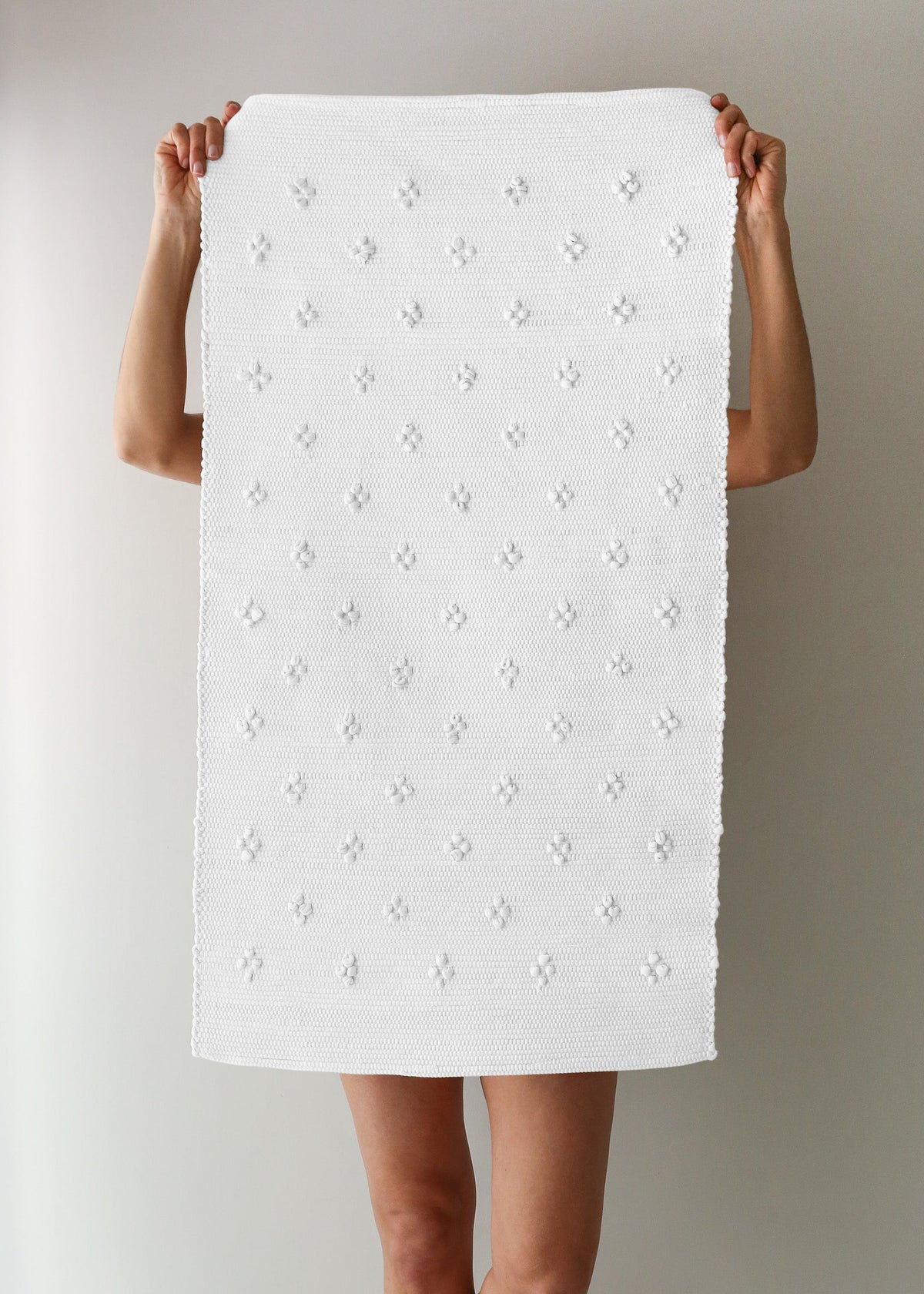Person holding a white textured bath mat against a plain background