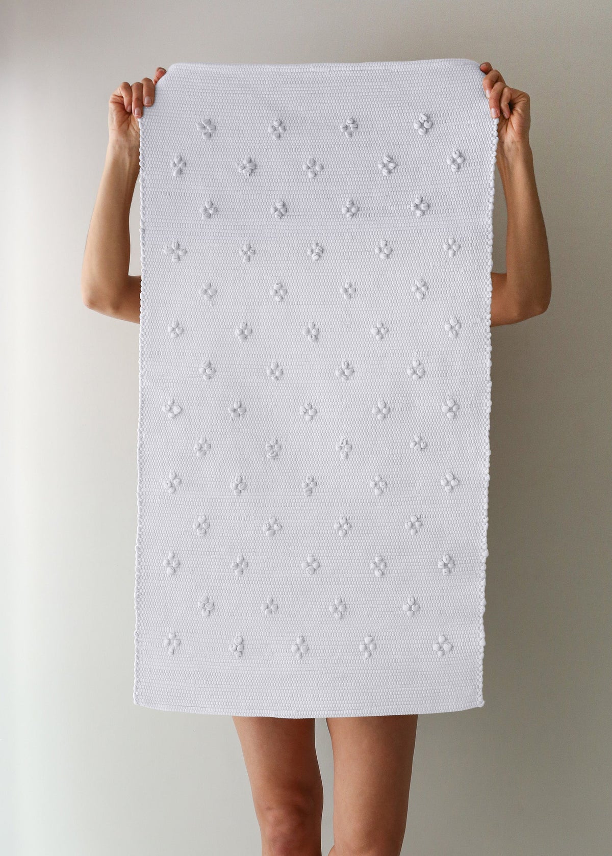 Person holding a white textured bath mat against a plain background